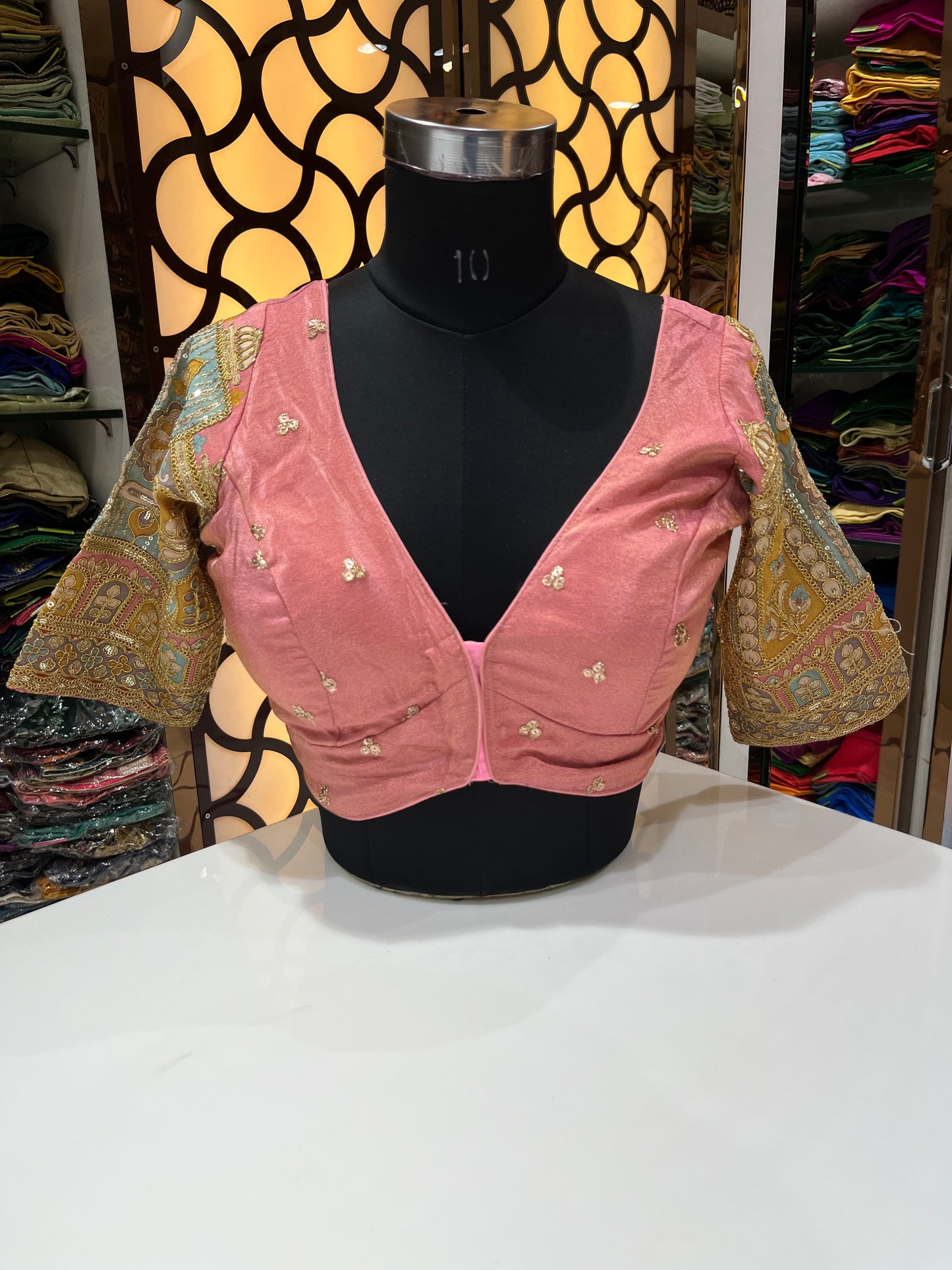 Elegant peach-pink designer blouse with a flattering deep V-neck and subtle golden butti work. Features beautifully embroidered statement sleeves for a rich, festive look—perfect for weddings and special occasions.
